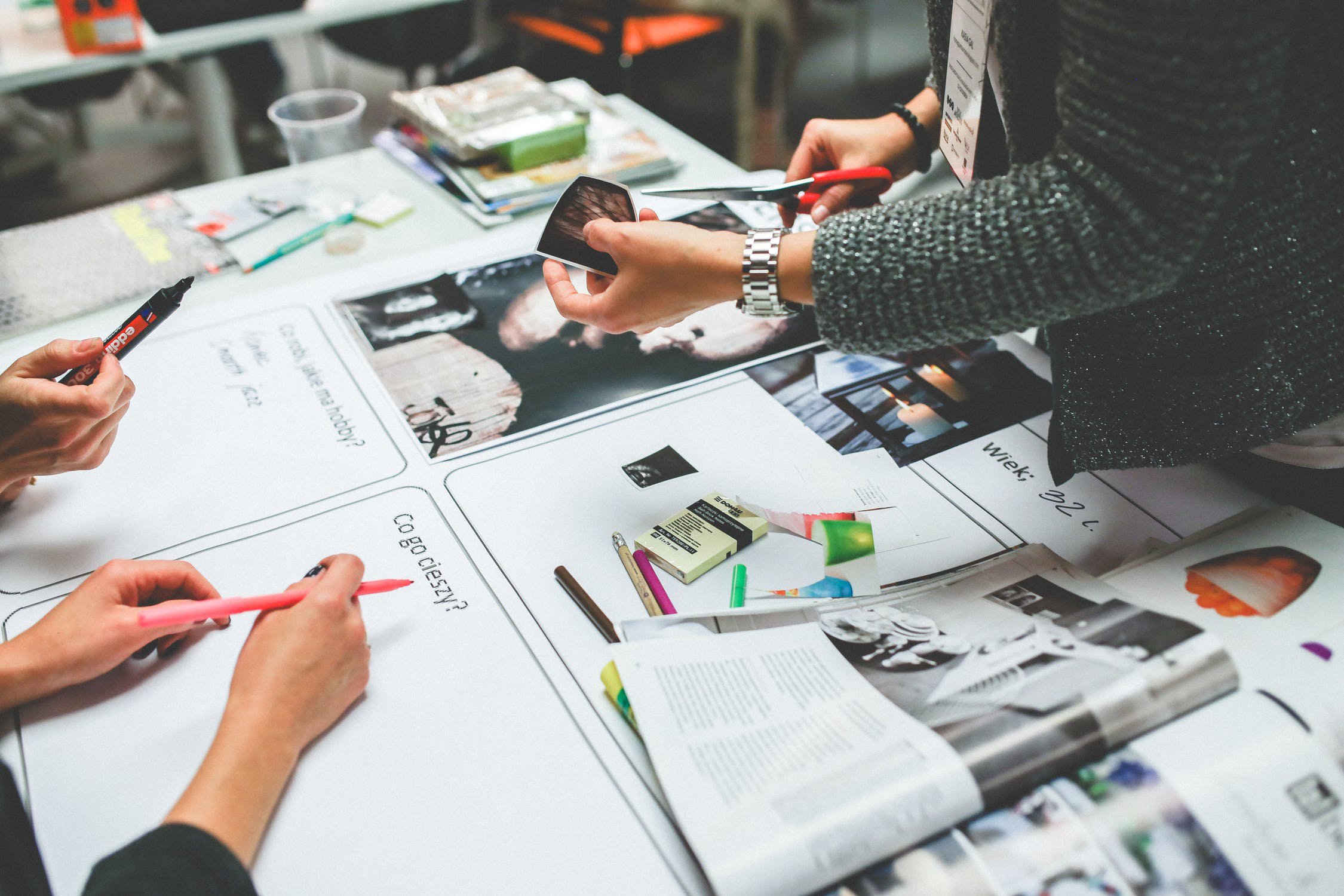 three people working on making a collage with pens and scissors in their hands