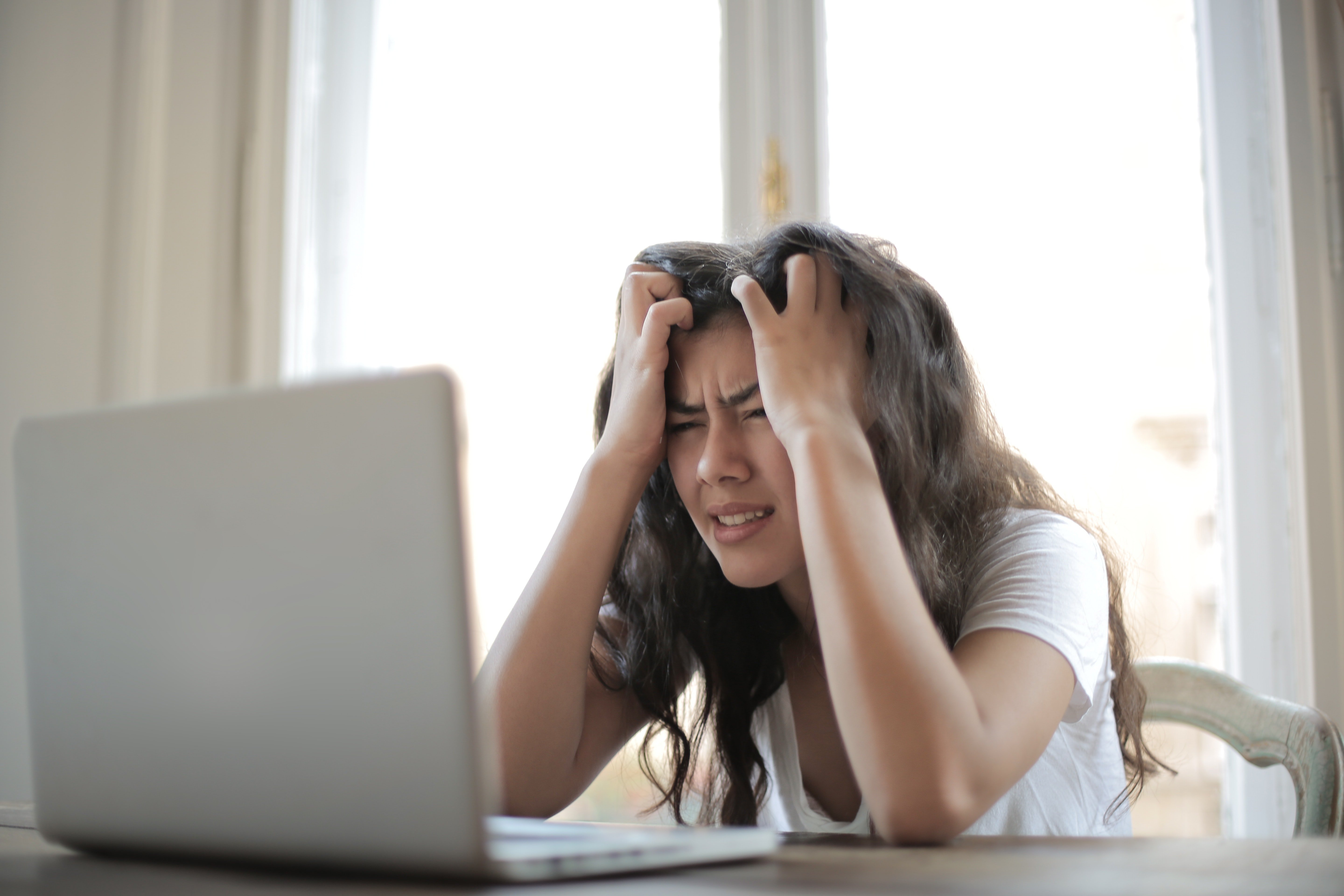 a woman holding her head in front of a laptop